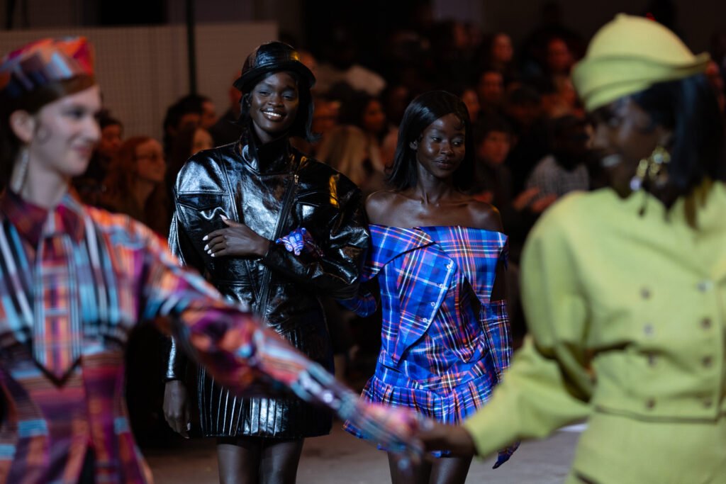 Models walk the runway in plaid looks during Tolu Coker at London Fashion Week (February 2026), with the audience in the background.
