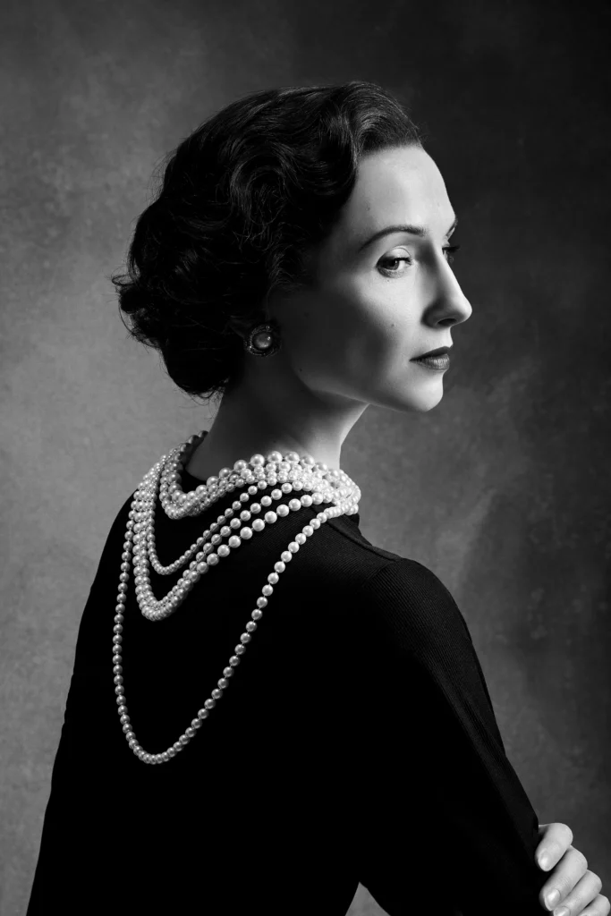 Black-and-white portrait of Svetlana Zakharova styled as Gabrielle Chanel, wearing layered pearl necklaces.