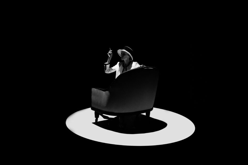 Black-and-white stage image of Svetlana Zakharova seated under a circular spotlight.