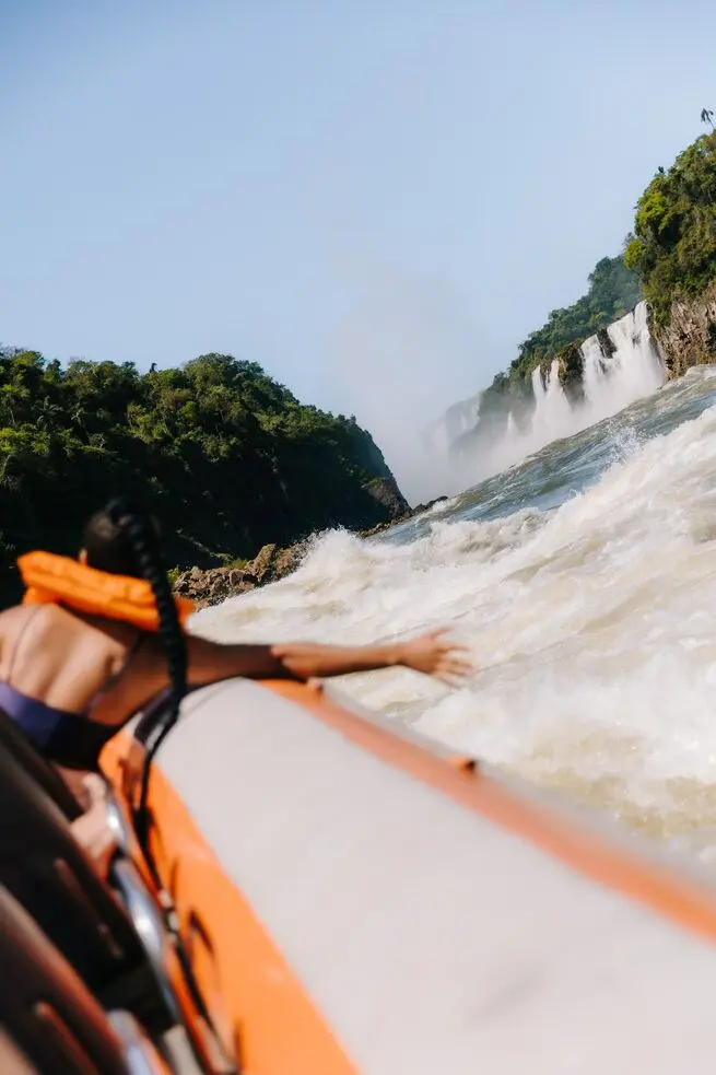 Passenger in an orange life jacket reaching towards the water during a Macuco Safari boat ride near Iguazu Falls.