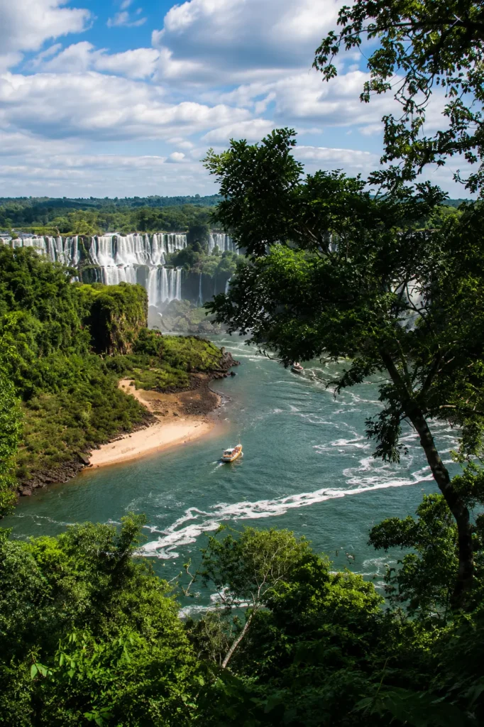 Iguazu Falls surrounded by the Atlantic Forest, with a small boat travelling along the river below.