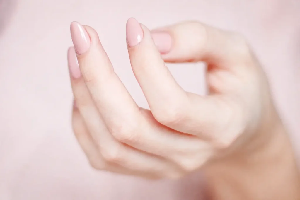 Close-up of a soft pink manicure with almond-shaped nails and a glitter accent nail