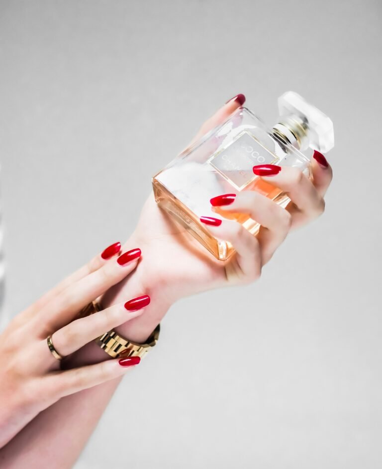 Close-up of hands with red nails holding a clear perfume bottle